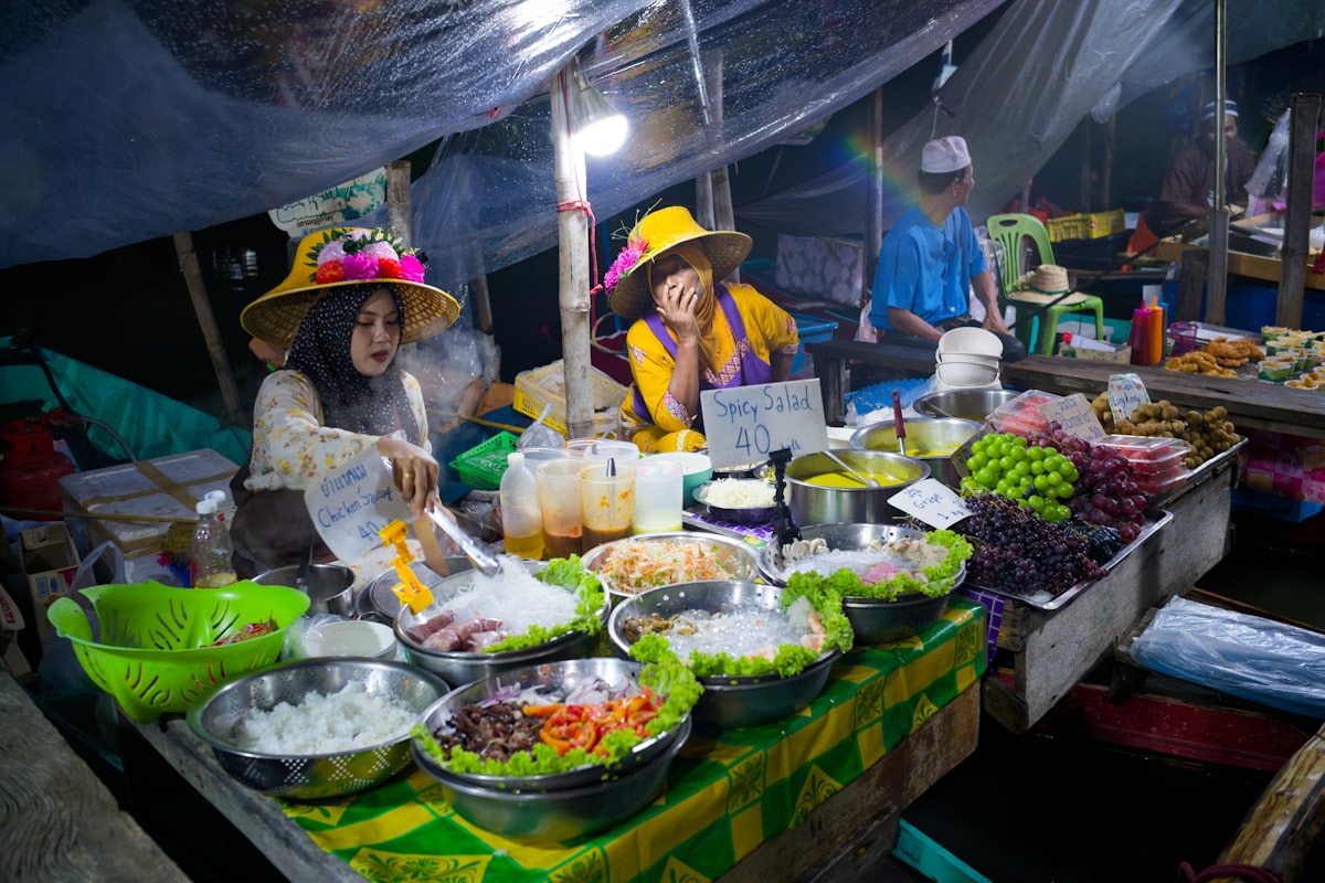 Vendors at a colorful night market food stall surrounded by fresh produce and prepared dishes