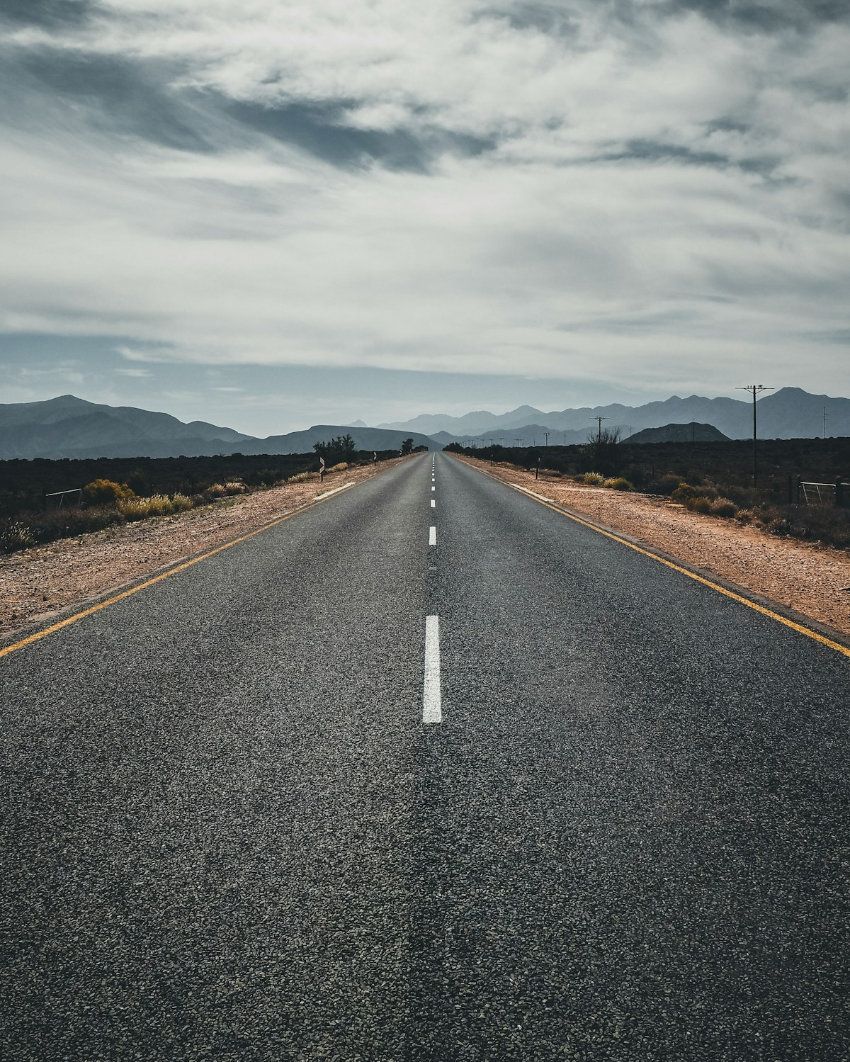 A long straight empty asphalt road running to the horizon through dry open country