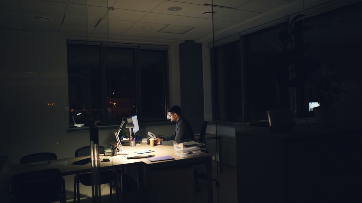 A man working alone, late, at a dimly lit office desk