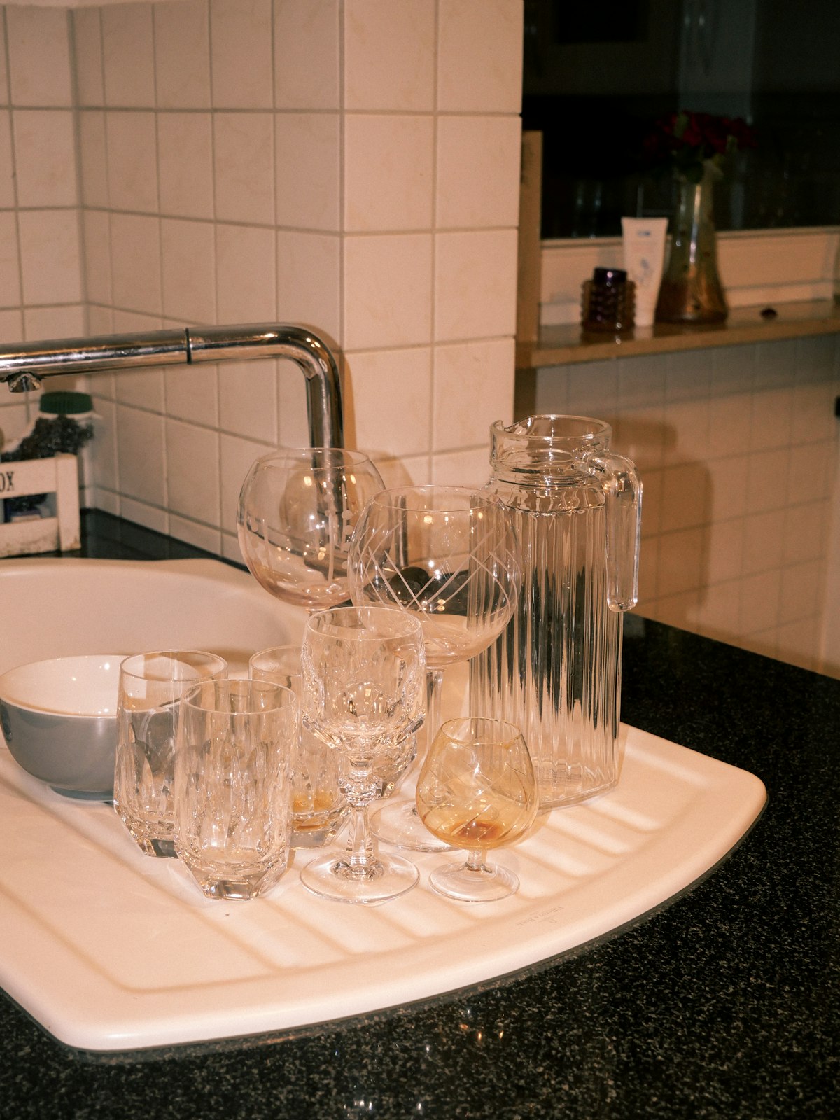 Empty glasses and a bowl gathered by a kitchen sink after a gathering