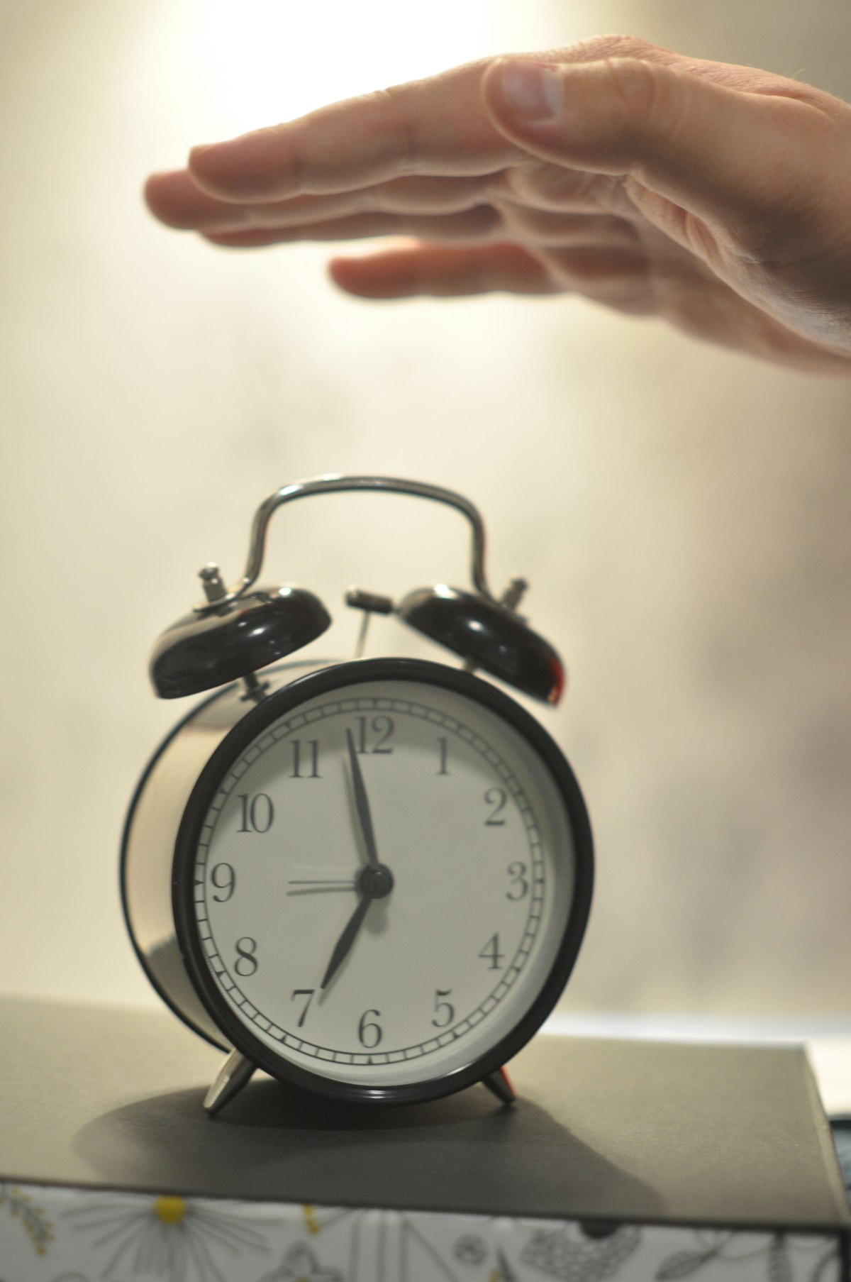 A hand reaching down to silence a ringing alarm clock on a nightstand in dim early morning light