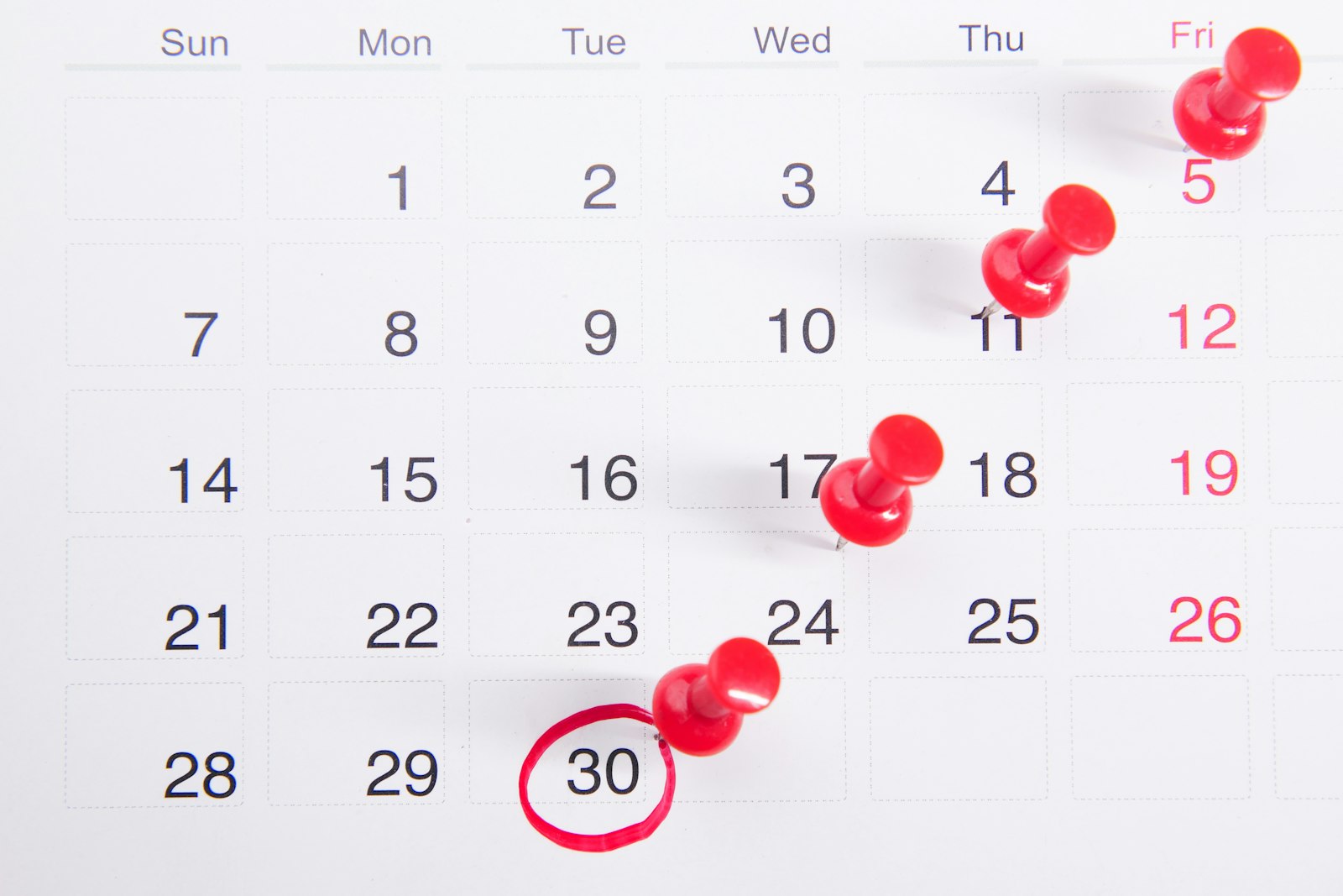 A wall calendar page with red pushpins marching diagonally across the dates and the 30th circled in red marker