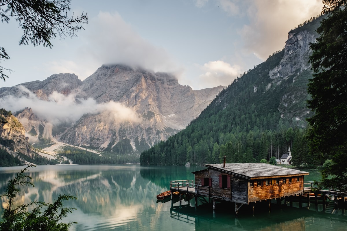 A small wooden cabin on a still alpine lake at dusk, mountains reflected in the calm water