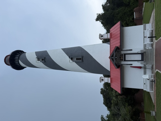 The full St. Augustine Lighthouse tower, red and white spiral, red-roofed keeper's house in front, under an overcast sky