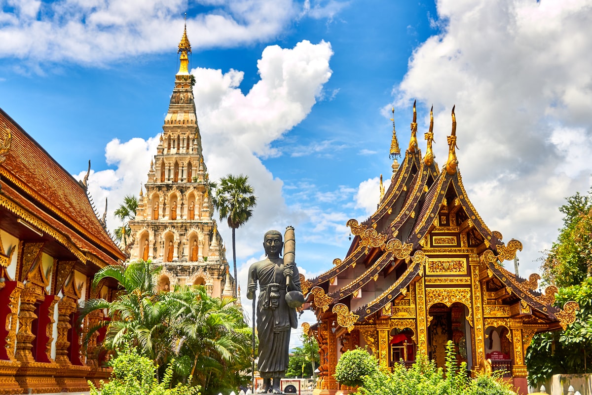 Golden spires and a standing Buddha statue at a northern Thai temple under a bright sky