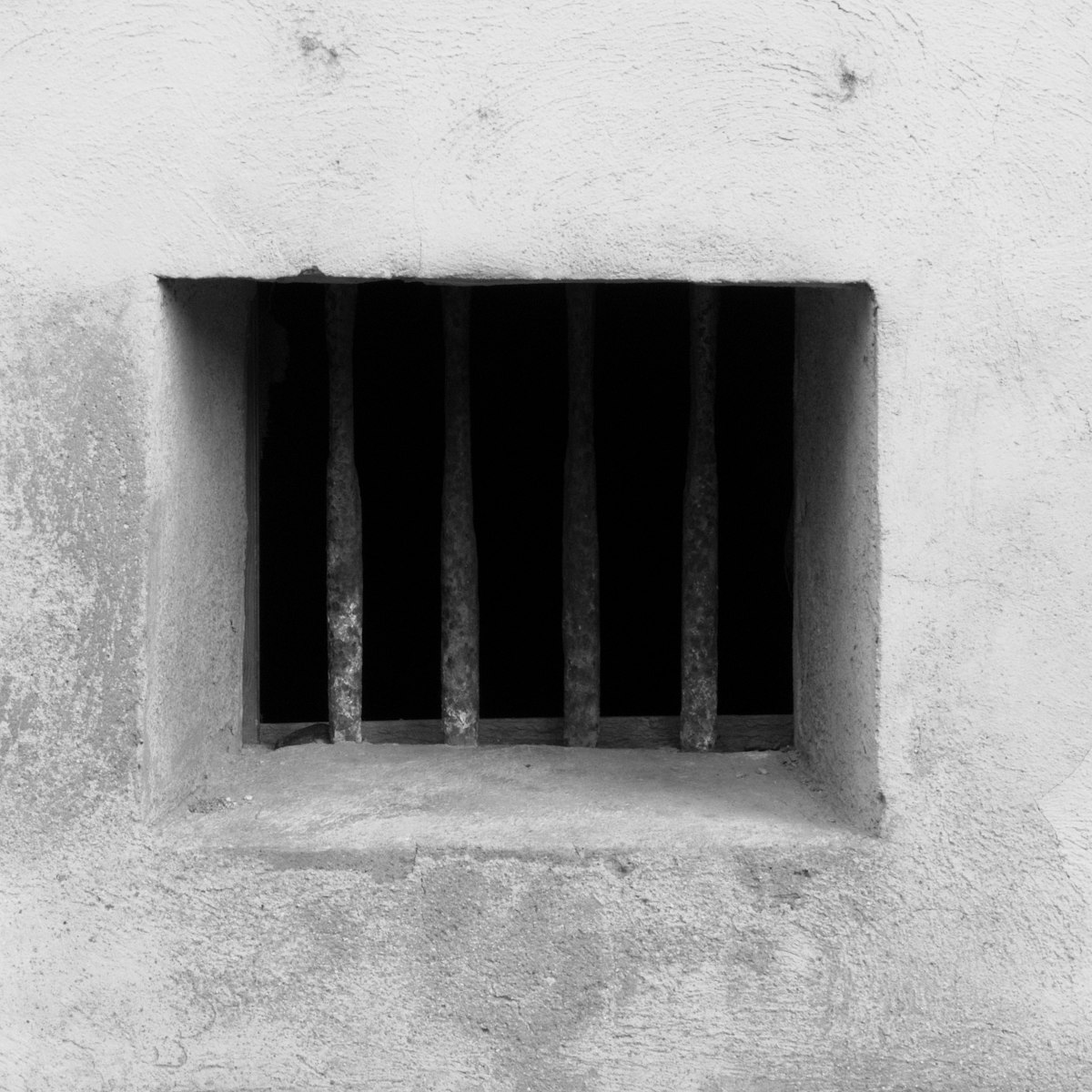 A small barred window cut into a stark concrete wall