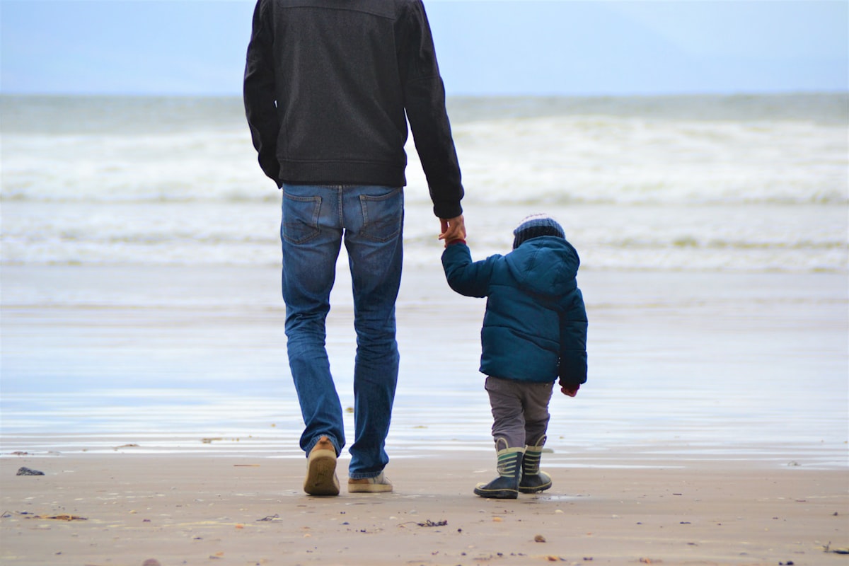 A father and young child walking hand in hand along a beach