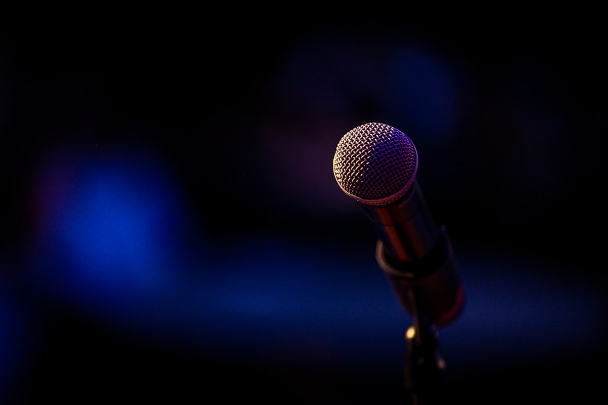 A single microphone on a stand, lit against a dark stage