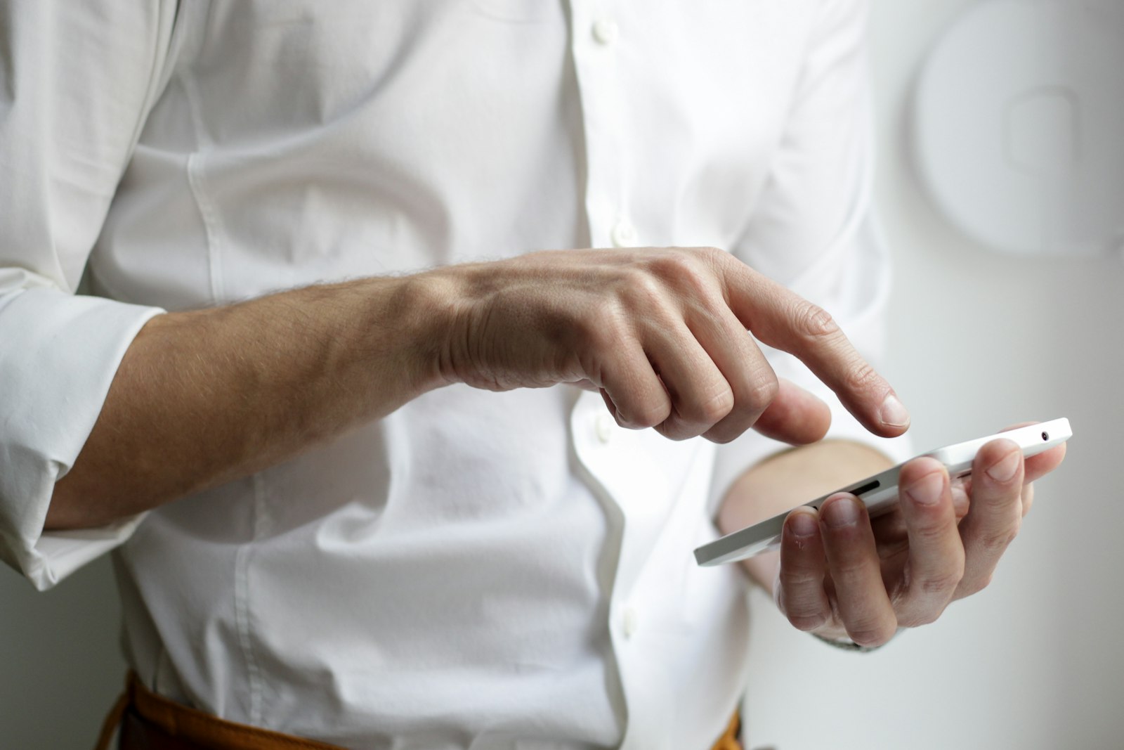 A close-up of a hand mid-tap on a smartphone screen, the person's shirt and background soft-focus with only the tapping hand in sharp focus