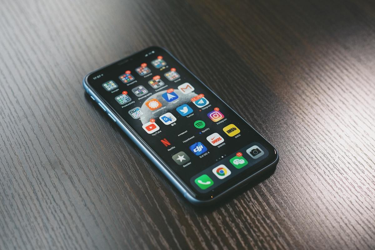 A smartphone lying face-up on a dark wood table, its home screen covered with apps showing notification badges