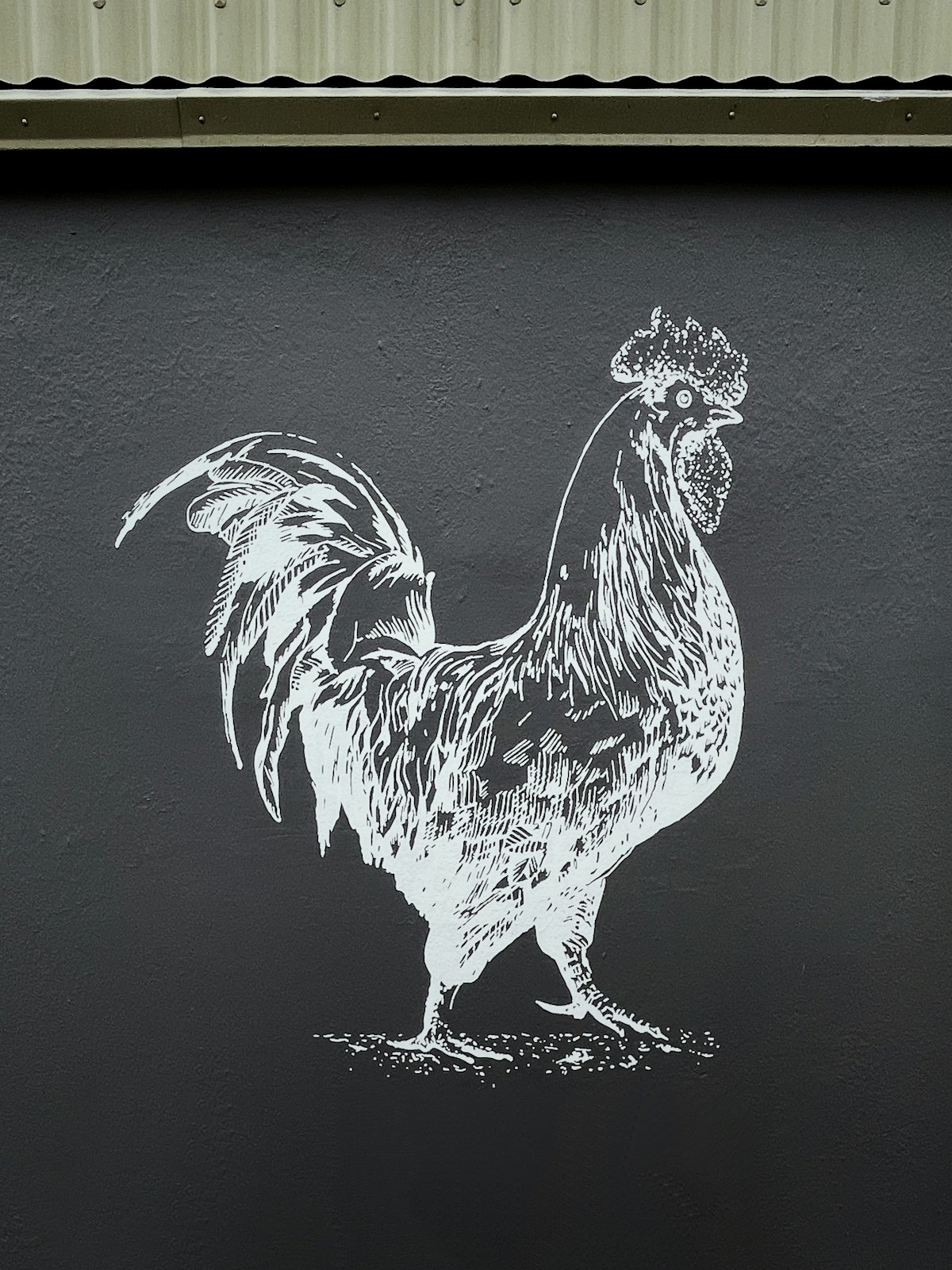 A stylized white illustration of a rooster painted on a dark wall, doodle-like in character