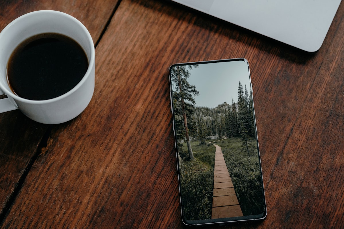 A phone left face-down on a wooden table next to a cup of coffee