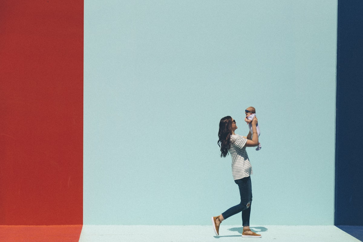 A mother lifting a swaddled newborn baby up against a bright wall