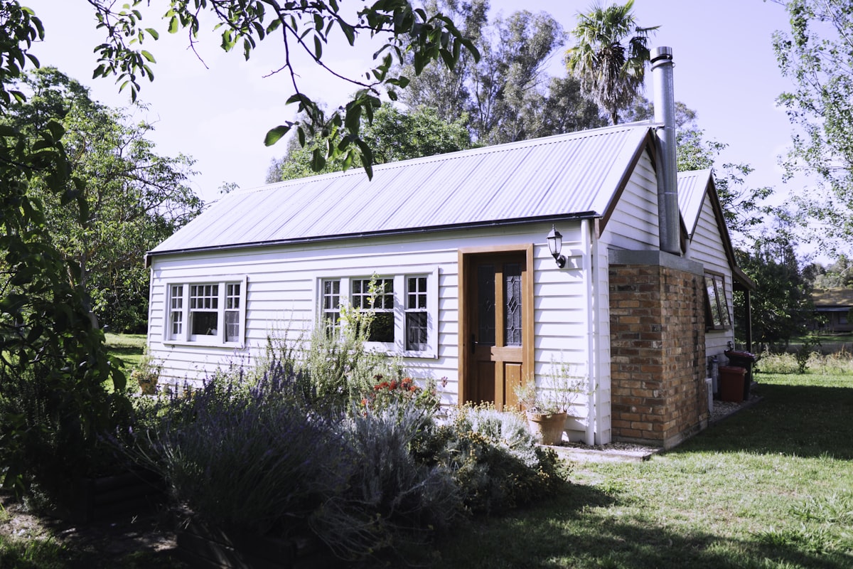 A small, plain white bungalow with a metal roof and a modest front garden